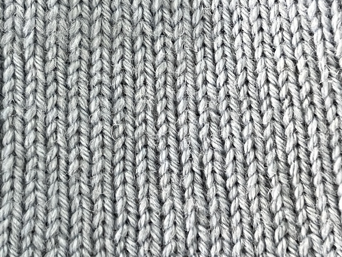 A stockinette stitch swatch in cream yarn, lit softly on a table