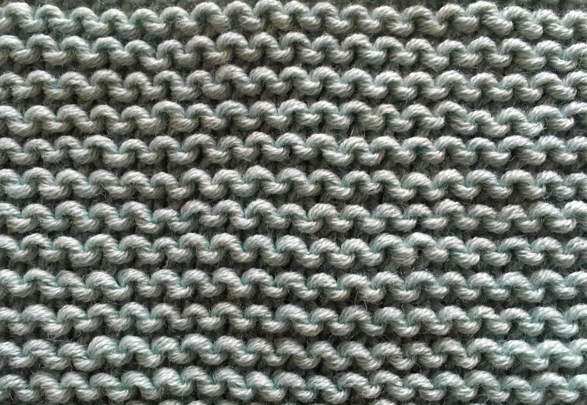 A garter-stitch swatch of cream yarn on a wooden surface